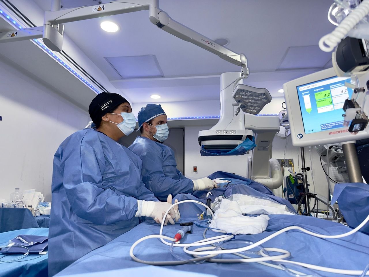 Two surgeons in blue scrubs and masks performing a minimally invasive procedure in a modern operating room with surgical monitors and equipment.